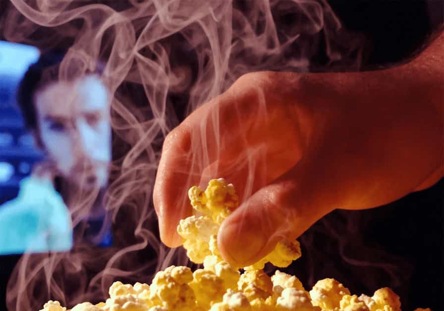Close-up of a hand reaching into bright movie theater popcorn, illustrating how combined senses (sight, smell, taste, touch) enhance flavor perception.