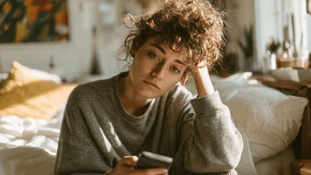 A mentally exhausted person sitting quietly with a phone after prolonged online interactions.
