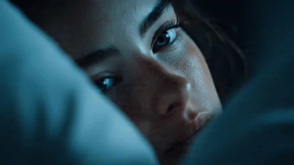 Young adult girl lying awake in bed at night with a thoughtful expression, representing overthinking and racing thoughts