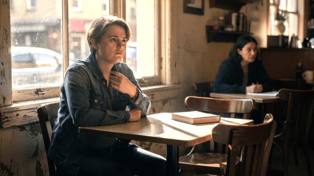 Person in a café looking uncomfortable as someone glances from nearby, illustrating the psychological unease of being watched.