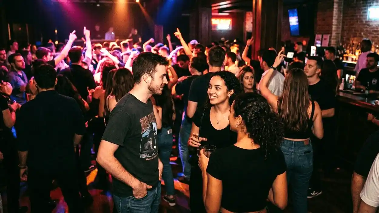 A crowded nightclub dance floor, one person approaching another at a 45‑degree angle with open body language, both making eye contact.