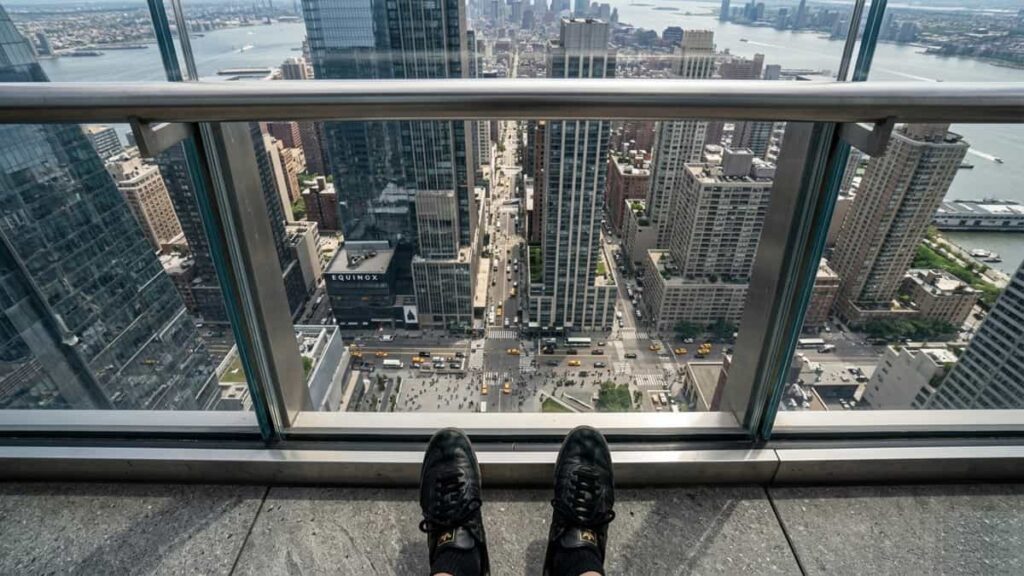 First-person view looking down from a tall observation deck over a city, showing height awareness and vertigo sensation