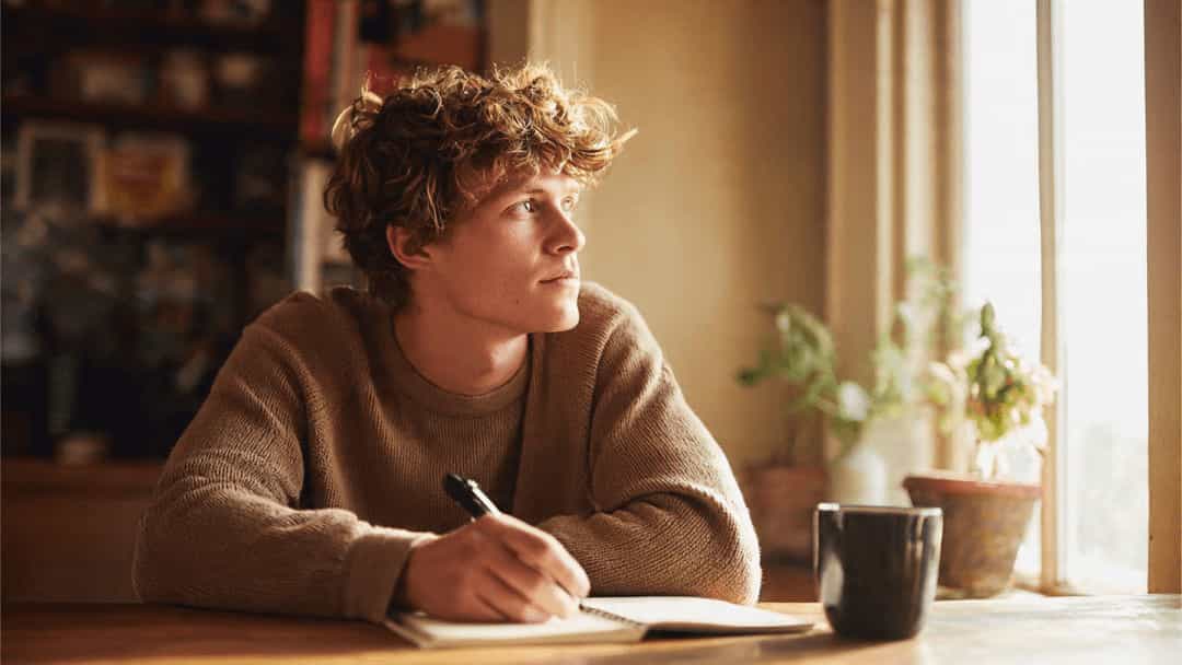 Young man sitting at a desk with a notebook and pen, practicing self-reflection to recognize projection